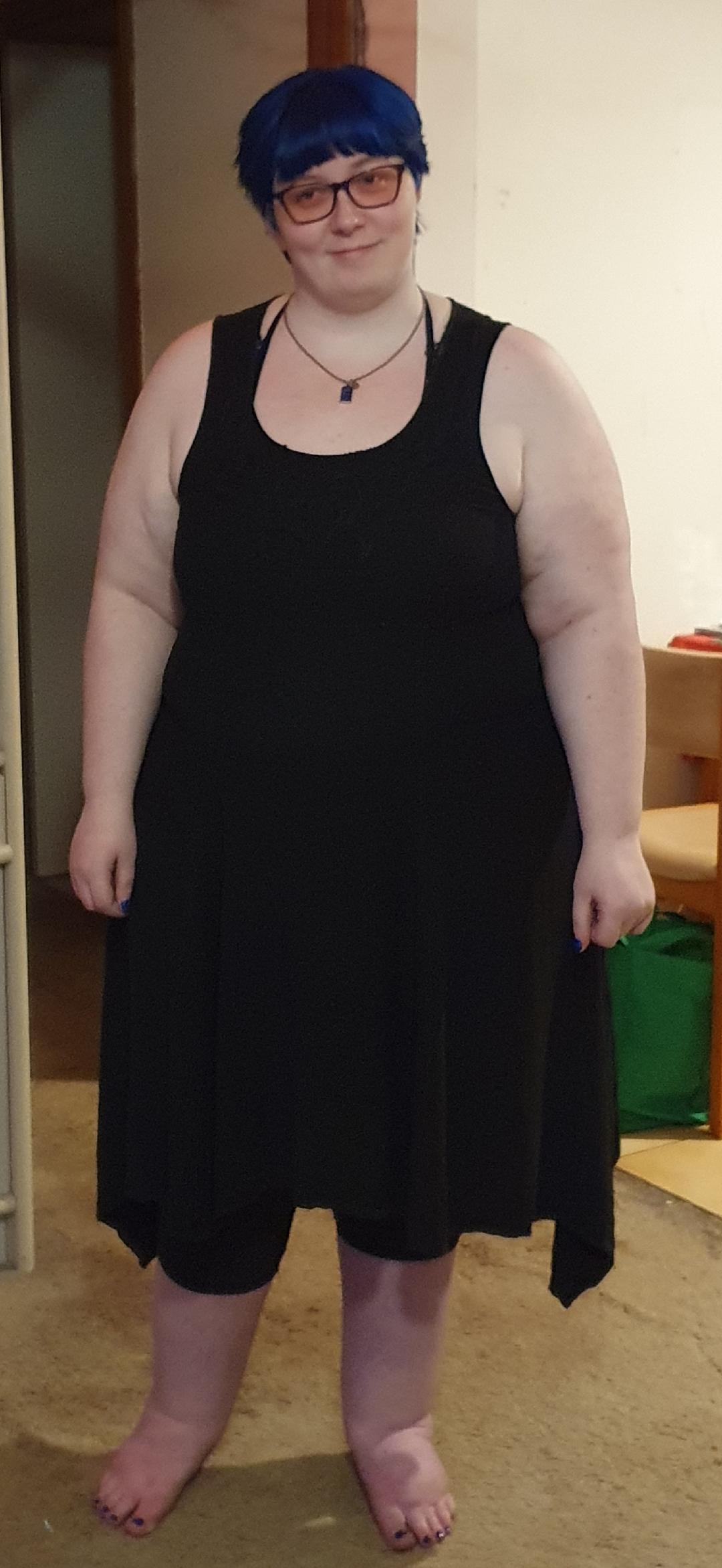 Blue short hair with black sleeveless dress and black leggings. wearing a Tardis necklace