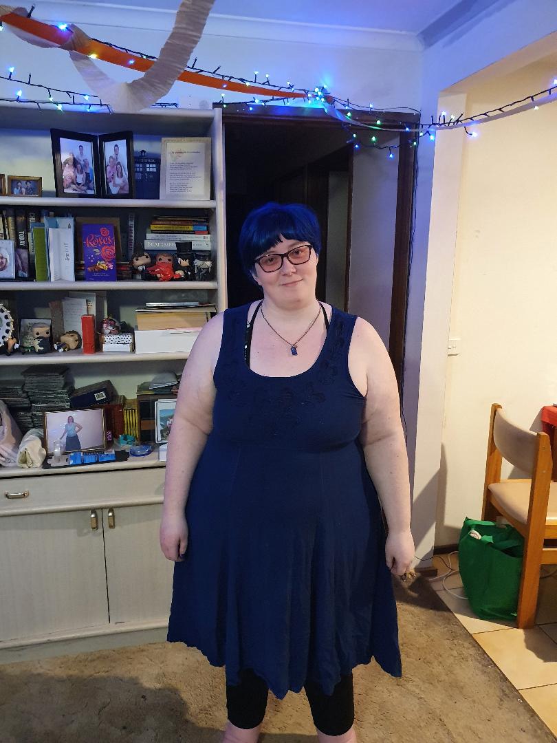 Blue short hair with blue sleeveless dress and black leggings. wearing a Tardis necklace